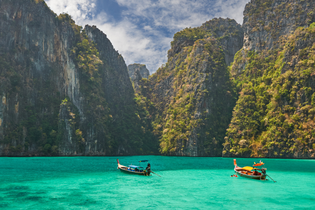 Longtail Boats sailing through limestone cliff in Thai islands